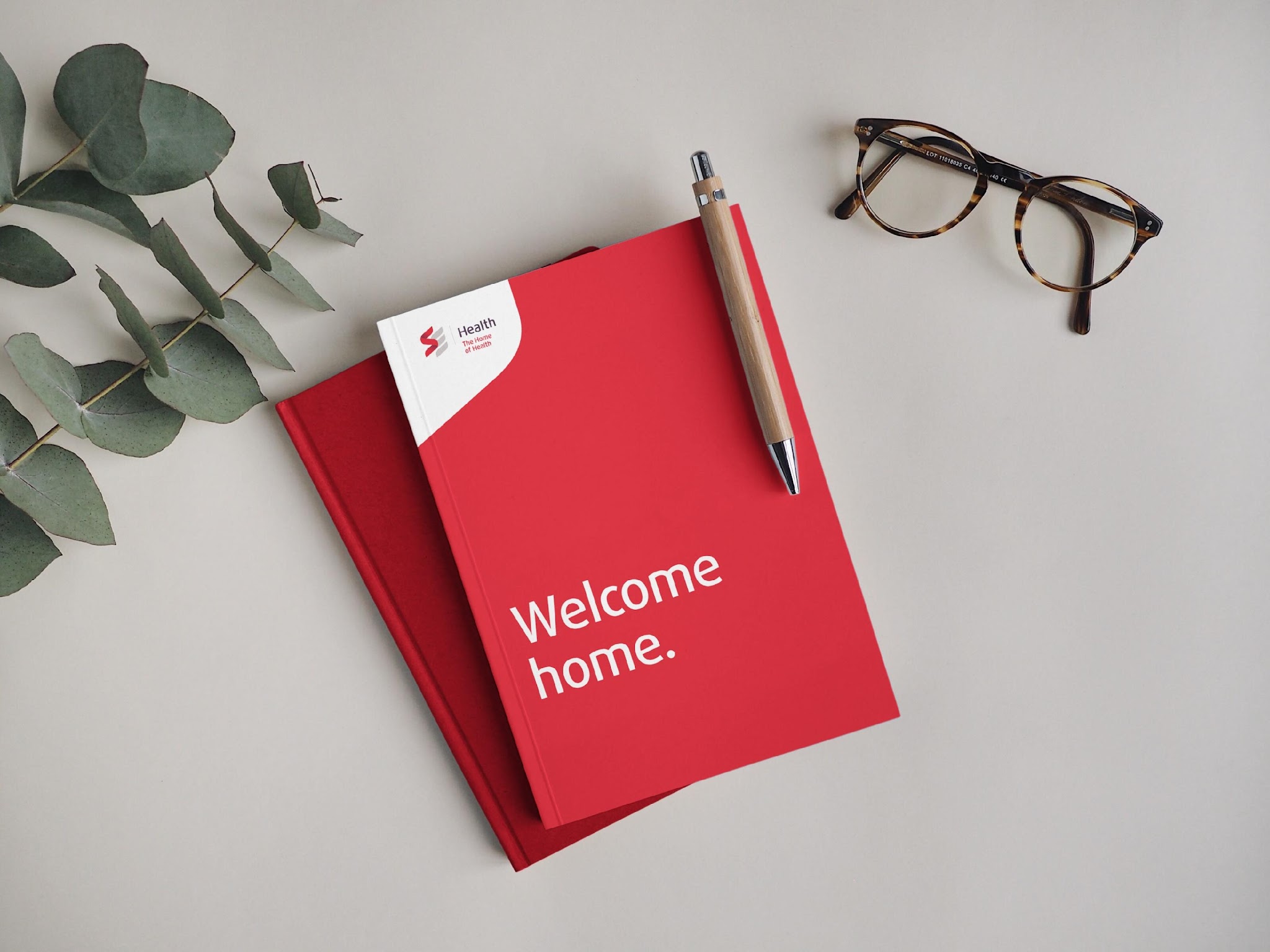 &lsquo;Welcome home.&rsquo; red notebook flatlay with eyeglasses and eucalyptus , SE Health stationery.
